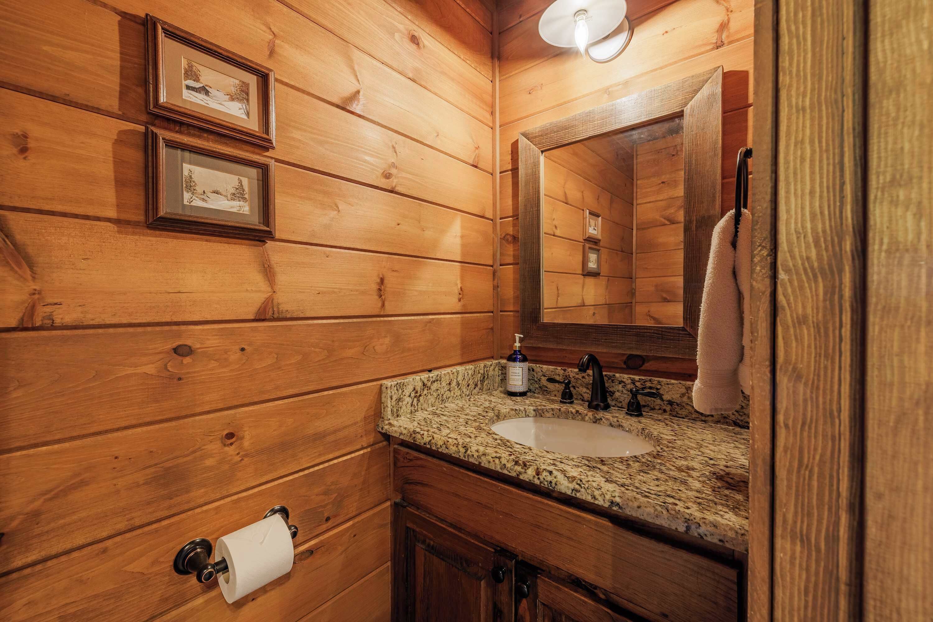 A wooden cabin-style bathroom with a granite countertop sink, a mirror, and framed pictures on the wall.