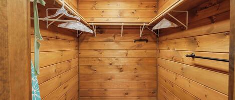 A wooden cabin interior with a sloped ceiling, wooden walls, a metal clothes rack, and a vent on the ceiling.