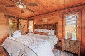 A wooden room with a bed, a nightstand, a ceiling fan, and a window with blinds. - Family Mountain Cabin in Blue Ridge, GA | Prime Fall Leaf Views1 (Blue Ridge)