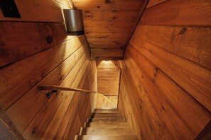 A wooden staircase leading to a higher level, with a metal handrail and a light fixture on the wall.