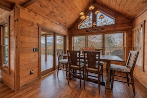 A wooden cabin interior with a dining table, chairs, and a view of the outdoors through large windows. - Family Mountain Cabin in Blue Ridge, GA | Prime Fall Leaf Views1 (Blue Ridge)