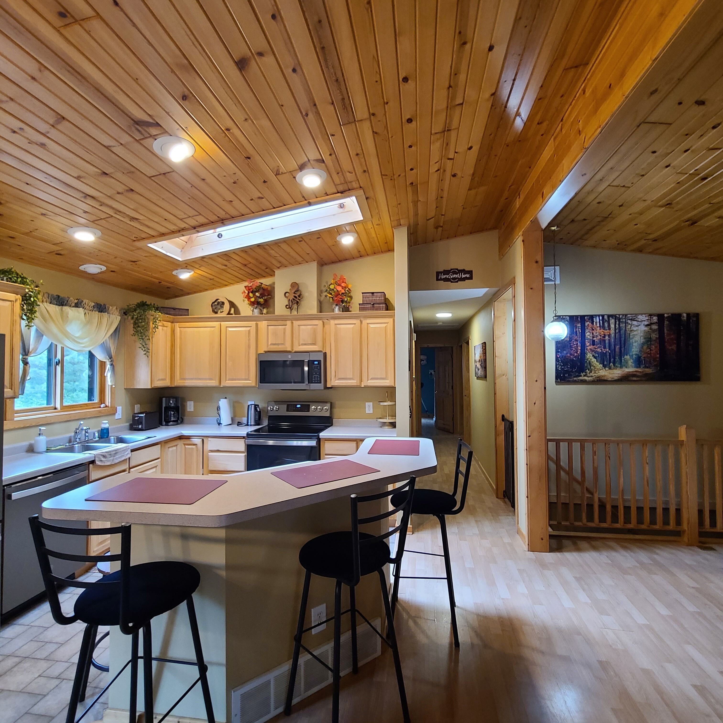 Une cuisine avec des meubles de rangement en bois, un îlot central doté de tabourets, un four à micro-ondes et une cuisinière.