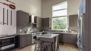 A modern kitchen with dark cabinetry, a large window, a central island with stools, and a wine rack on the wall. - Large Modern Home in Squamish (Squamish)