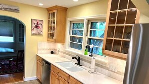 A kitchen with wooden cabinets, a stainless steel refrigerator, a double sink, and a window with a view of greenery outside. - 1950's Brick House. Tons of character. Minutes from downtown Meridian. (Meridian)