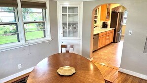A dining area with a wooden table and a single plate, a white door with a window, and a kitchen visible through an archway. - 1950's Brick House. Tons of character. Minutes from downtown Meridian. (Meridian)