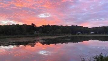 A calm lake reflecting a sunset sky with trees and buildings in the background.