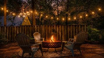 A fire pit with chairs, surrounded by a wooden fence and string lights.