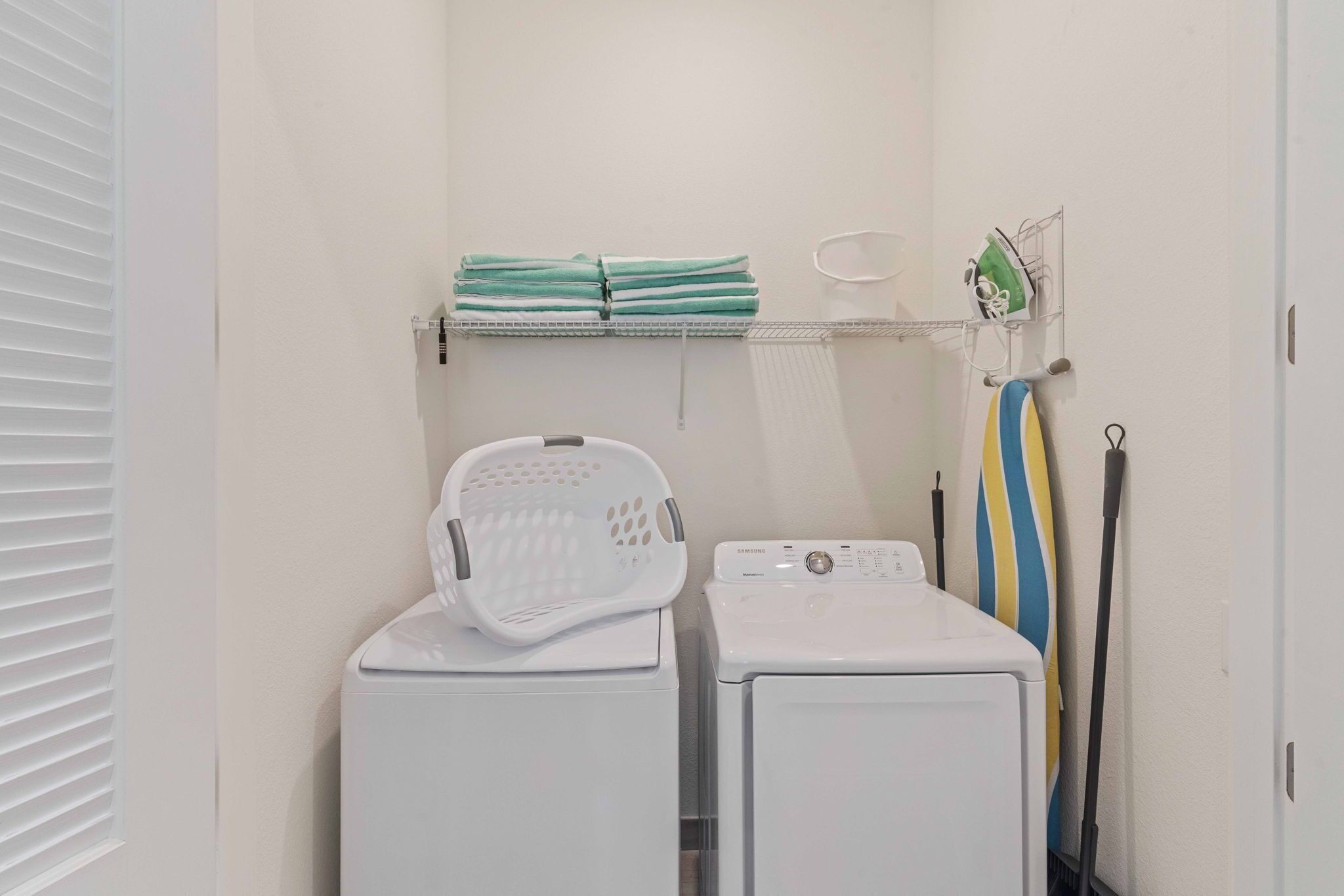 Un espace buanderie comprenant deux machines à laver blanches, un panier à linge blanc, une étagère avec des serviettes pliées et un porte-mop.