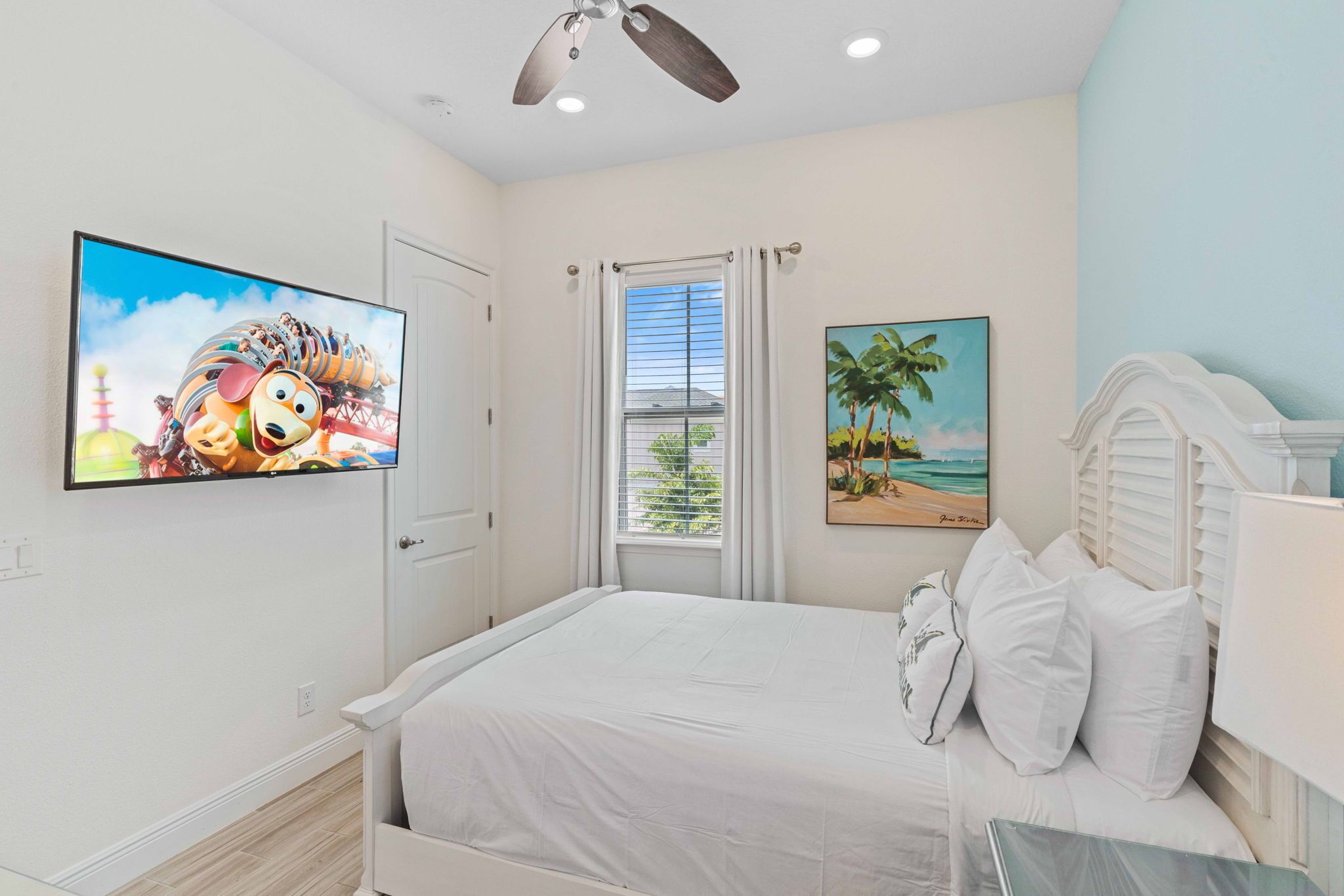 A bedroom with a bed, a ceiling fan, a window with curtains, and two wall-mounted pictures.