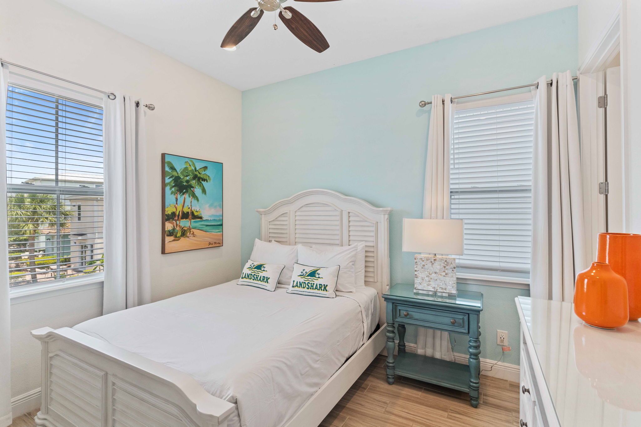 Quarto com cama, mesa de cabeceira, abajur e quadro de uma praia.