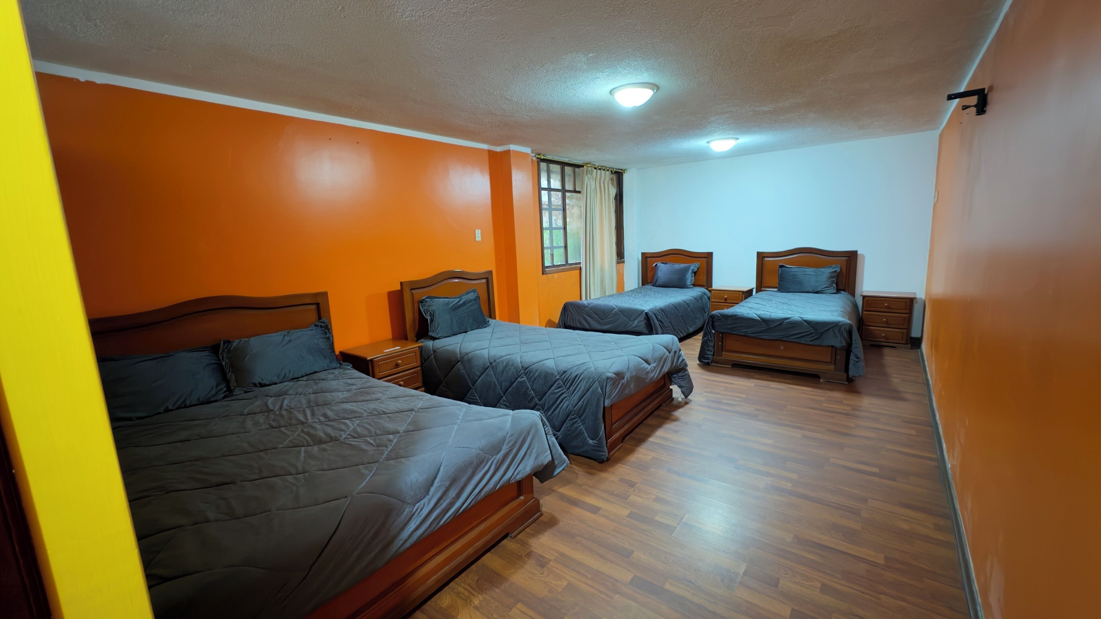 Una habitación con cuatro camas, cabeceras de madera y una ventana con cortinas.