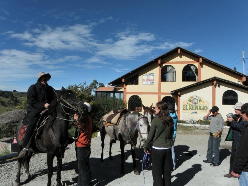 Un bâtiment sur lequel on peut lire l’inscription « Hôtel El Refugio », ainsi qu’une écurie où se trouvent des chevaux et des personnes.