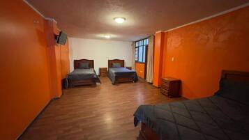 Quarto com duas camas, piso de madeira, paredes alaranjadas e janela com cortinas.