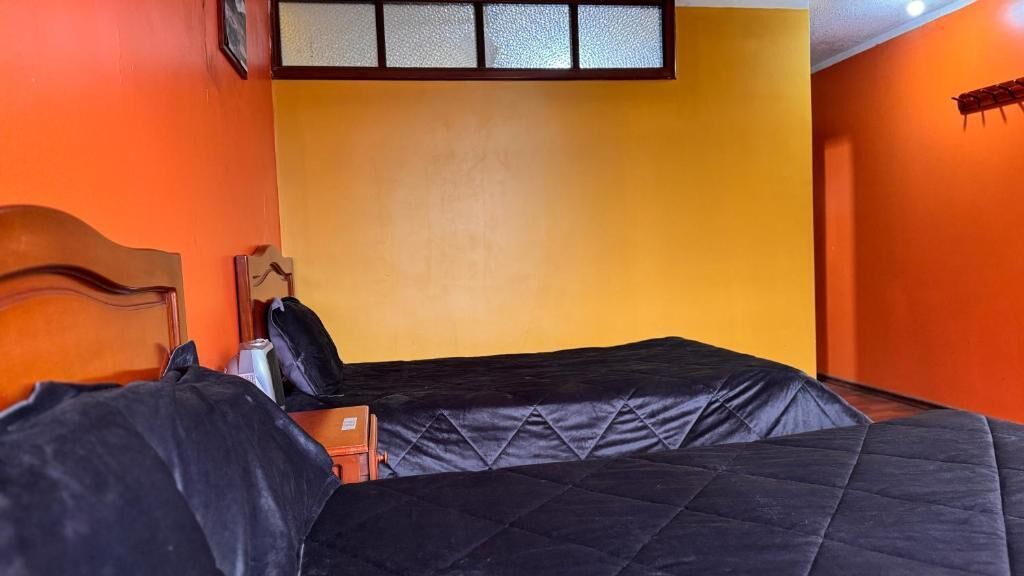 Habitació amb dos llits, un capçal de fusta, una taula petita i una prestatgeria penjada a la paret.