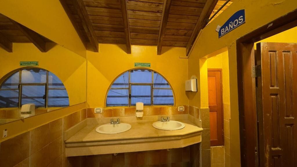 Un baño público con dos lavamanos, vigas de madera en el techo y un letrero que dice "BAÑOS".