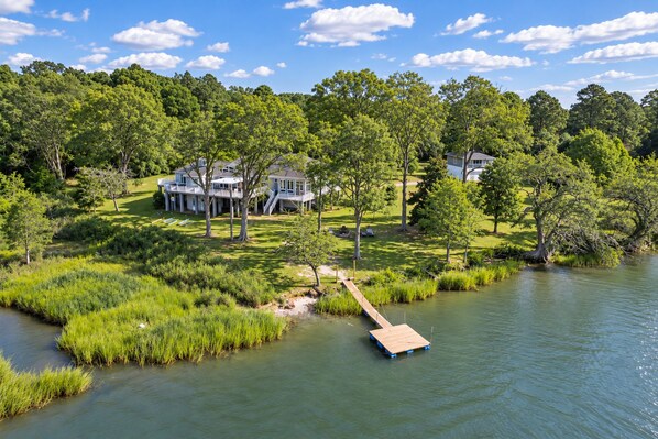 A lakeside property with a dock, grassy areas, and a house with multiple levels and a covered porch.