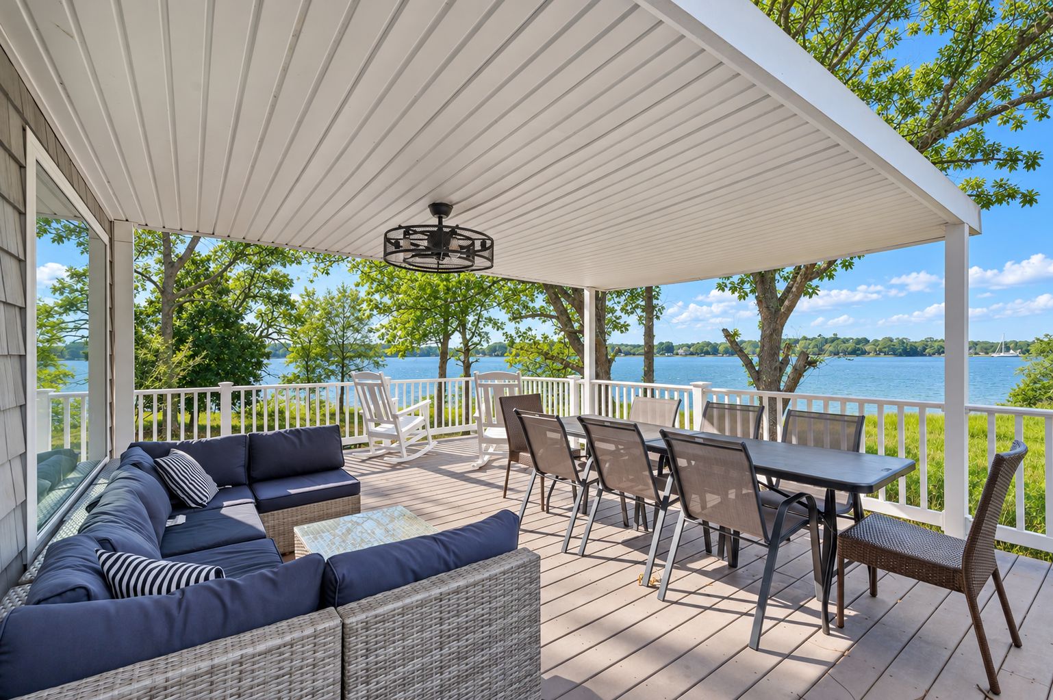 A covered outdoor deck with a sofa, chairs, and a table, overlooking a body of water.