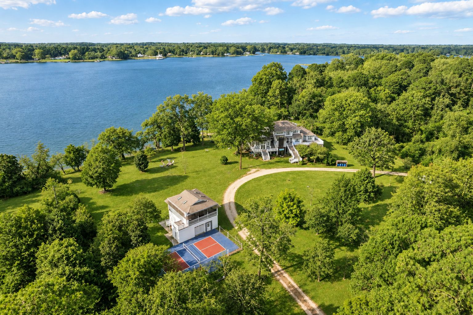 A large house with a tennis court, surrounded by dense trees and a lake.