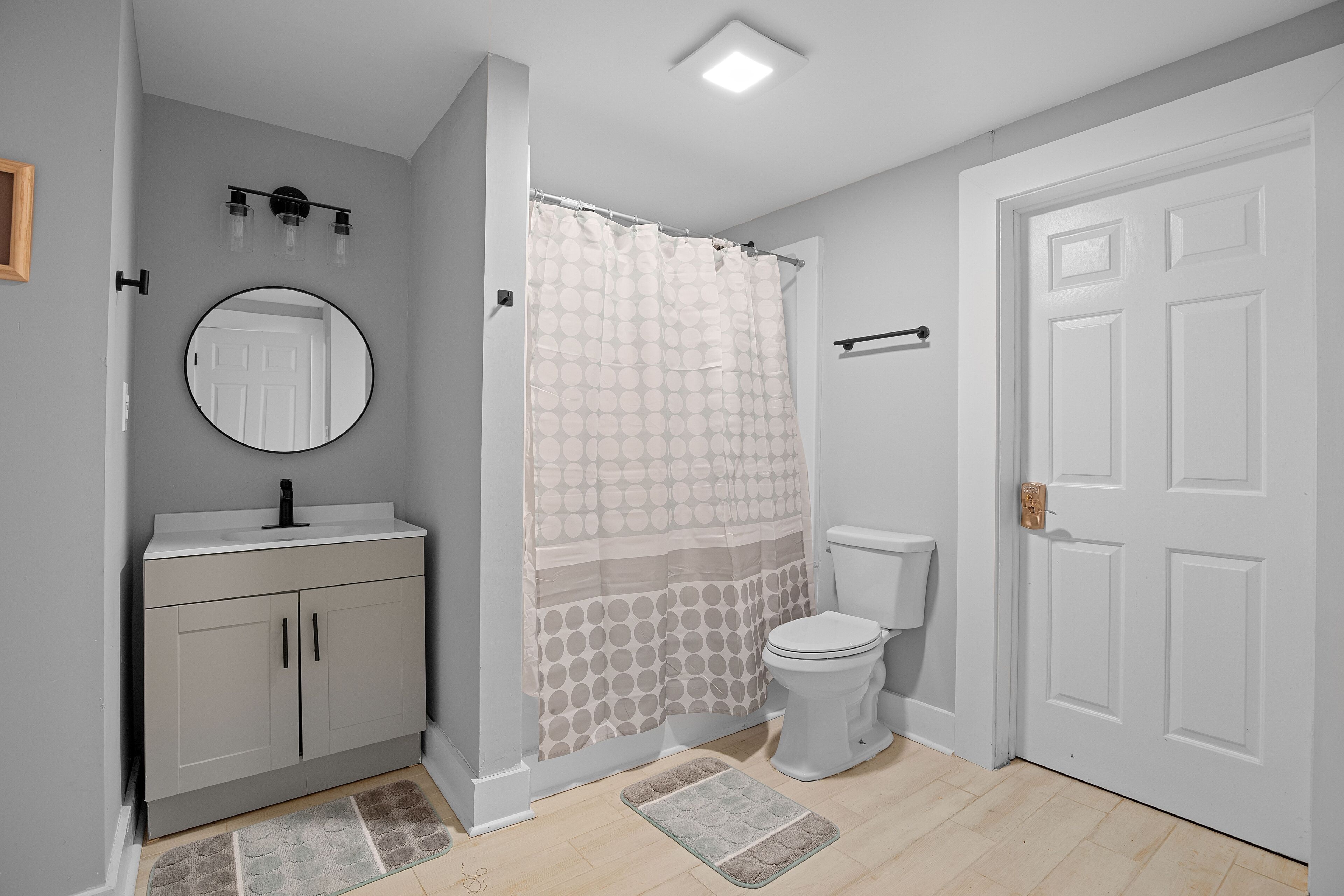A bathroom with a toilet, a sink with a mirror, a shower curtain, and a door.
