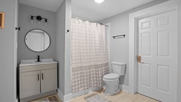 A bathroom with a toilet, a sink with a mirror, a shower curtain, and a door.