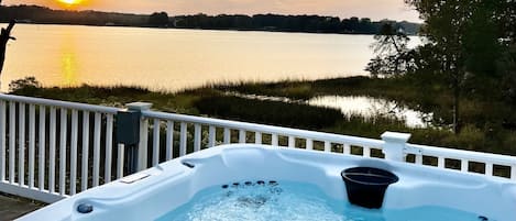 A hot tub on a deck with a view of a lake and sunset.