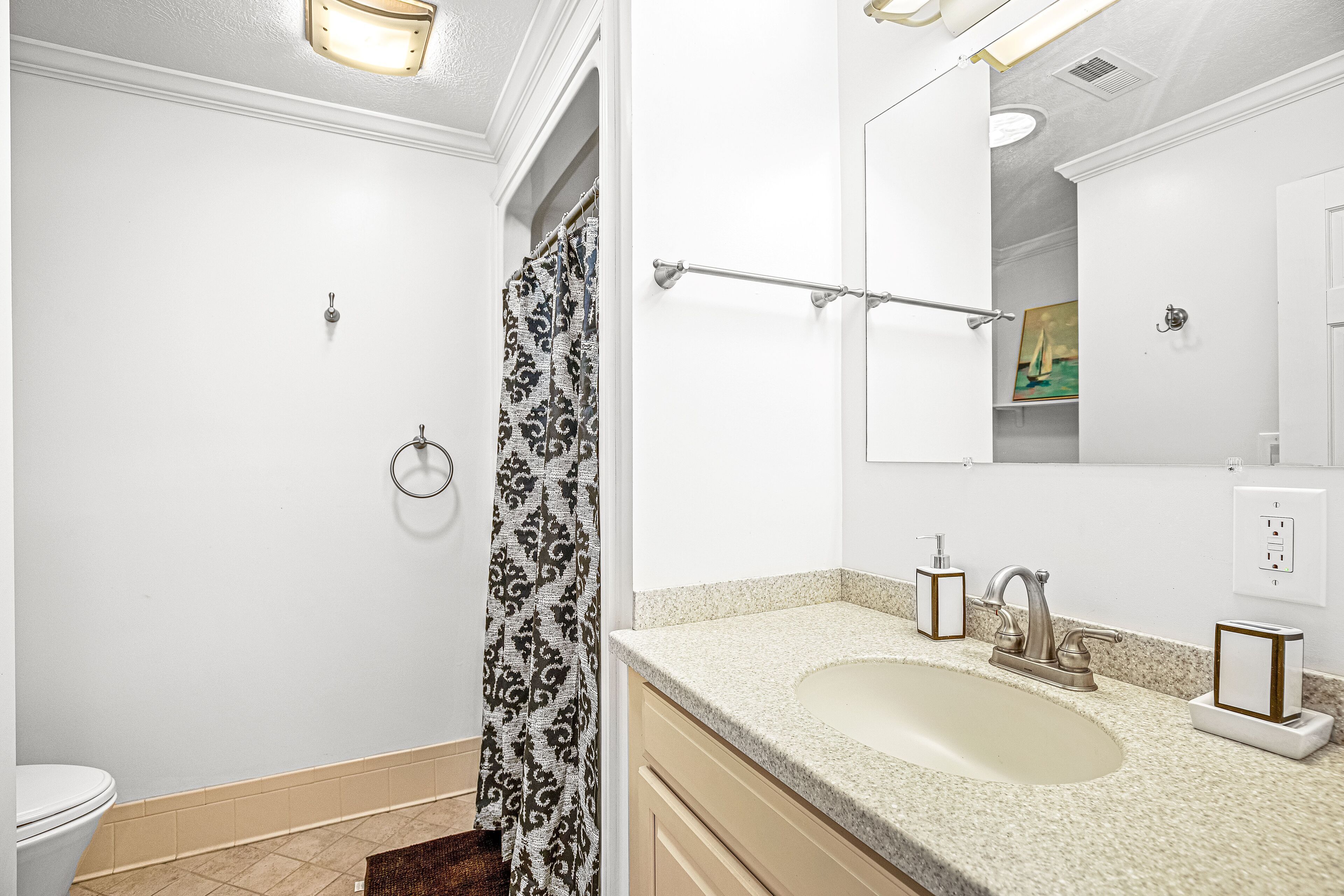 A bathroom with a toilet, shower curtain, sink, and mirror.