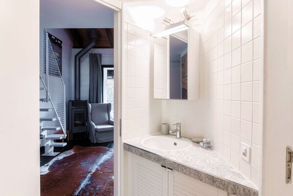 A modern bathroom with white tiles, a granite countertop, and a large mirror.