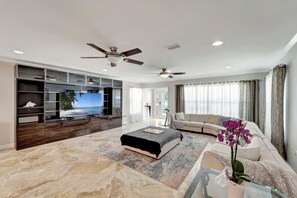 A modern living room with a large flat-screen TV, a sofa, a coffee table, and a ceiling fan. - Luxury House with Salted Heated Pool (Bradenton)