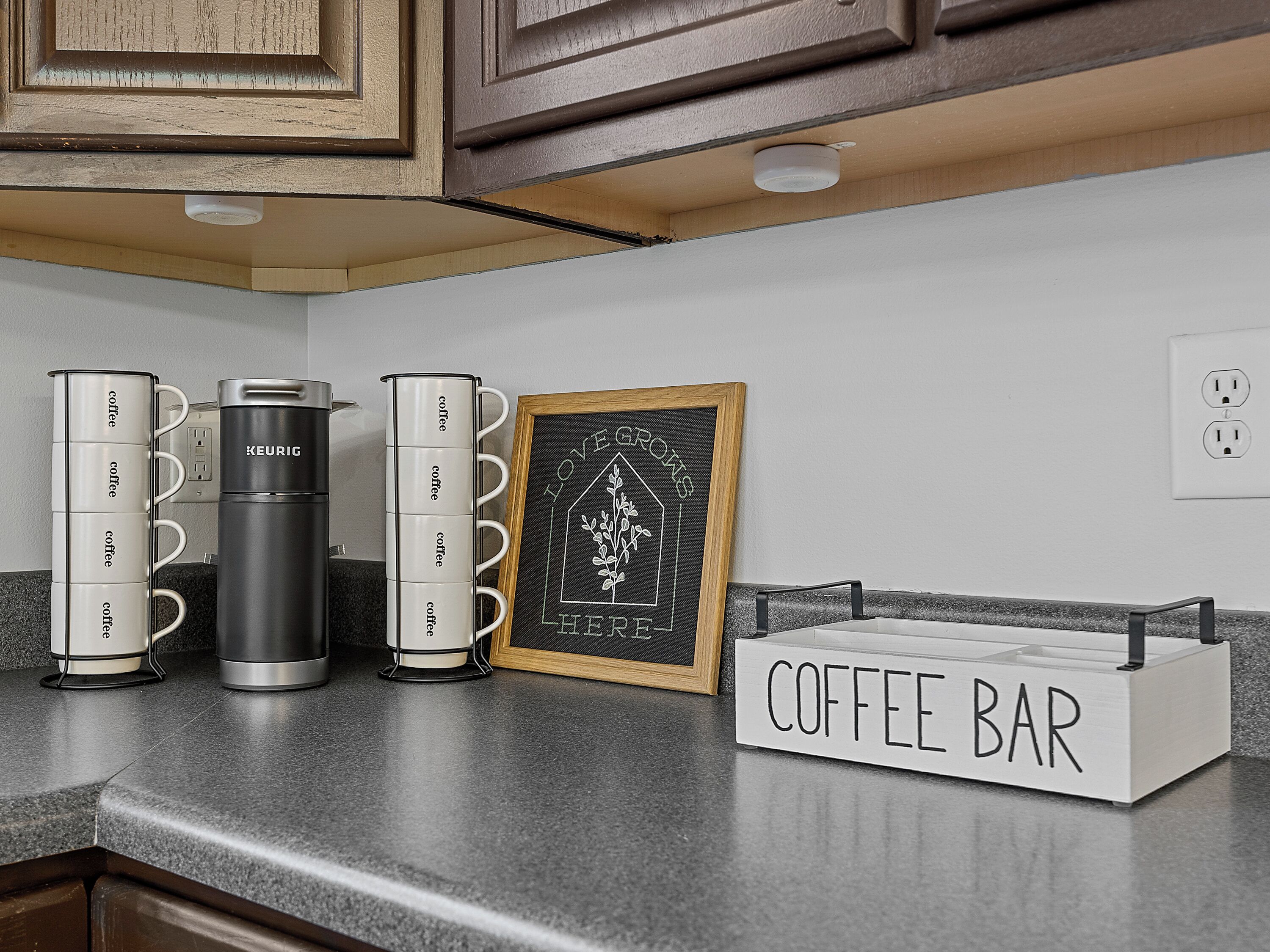 A kitchen counter with coffee makers, a chalkboard sign, and a coffee bar sign.