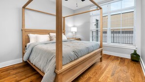 A four-poster bed with a wooden frame and a grey blanket, a ceiling fan, and a window with blinds. - Luxury Apartment over Target in Downtown Auburn - 208 (Auburn)