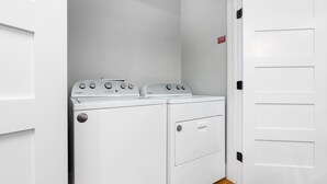 A laundry room with a Whirlpool washer and dryer, a white door, and a wooden floor. - Luxury Apartment over Target in Downtown Auburn - 208 (Auburn)