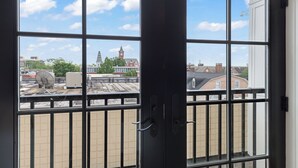A view from a window with a metal railing, overlooking a cityscape with buildings and a clock tower. - Luxury Apartment over Target in Downtown Auburn - 208 (Auburn)