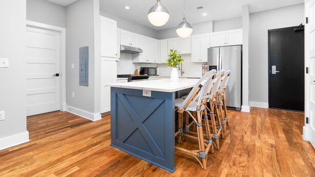 A modern kitchen with white cabinets, a blue island, and wooden flooring. - Luxury Apartment over Target in Downtown Auburn - 208 (Auburn)
