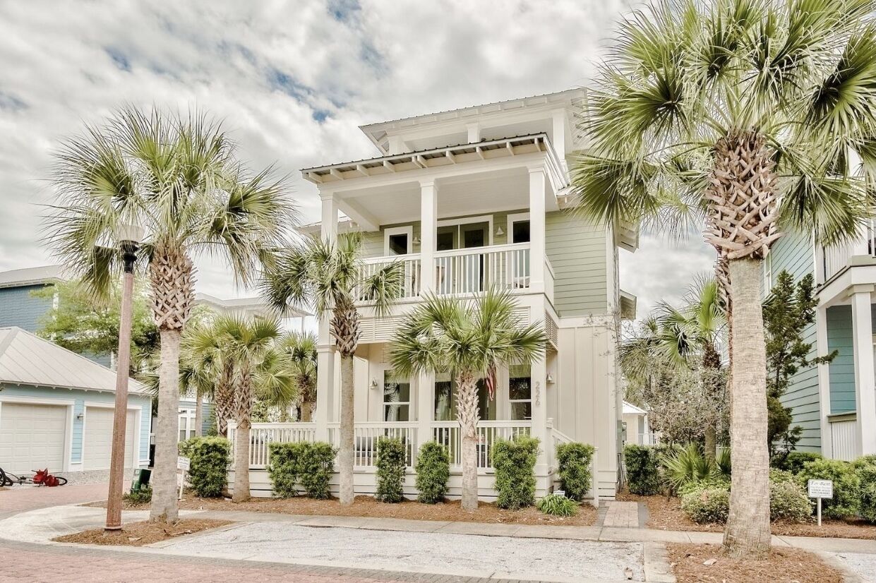 A two-story house with a porch, surrounded by palm trees and a well-maintained lawn.