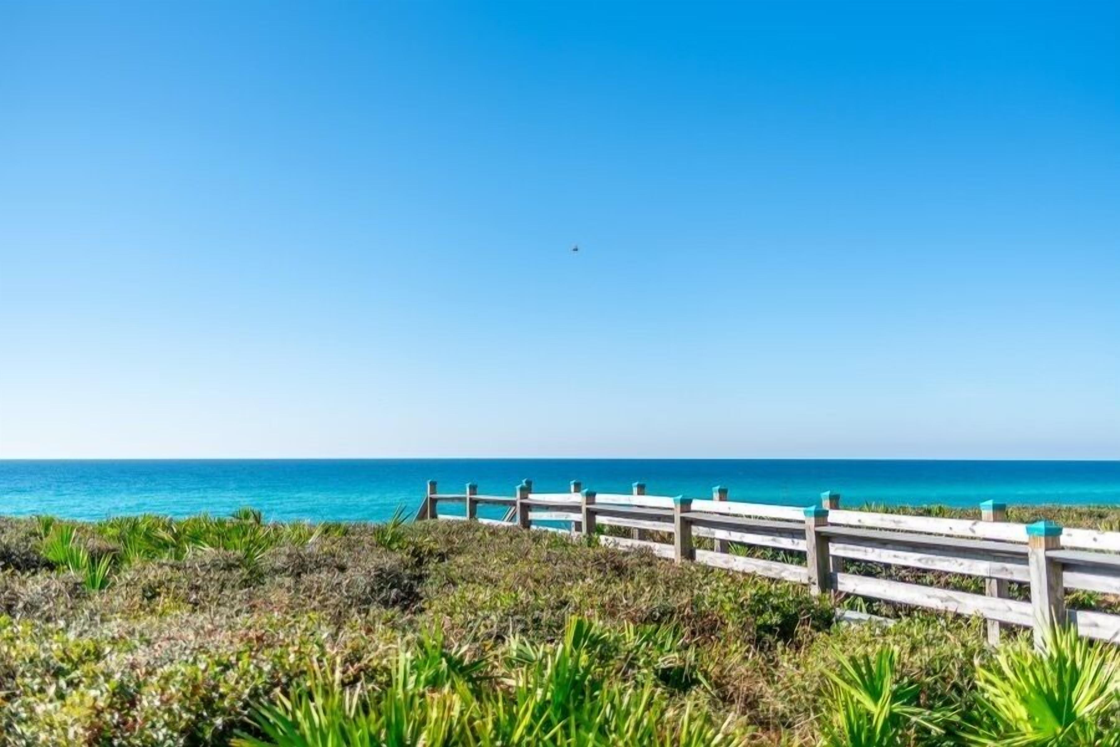 A wooden boardwalk leading to a beach with clear blue water and a clear sky.