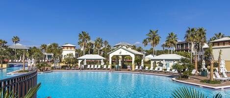 A large outdoor swimming pool surrounded by palm trees and lounge chairs.