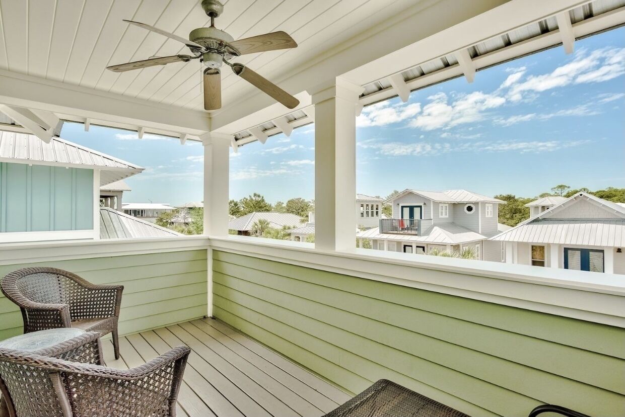 A covered porch with wicker furniture, a ceiling fan, and a view of neighboring houses.