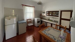 Cocina compacta con electrodomésticos básicos, comedor con una mesa estampada y ventana con cortinas.