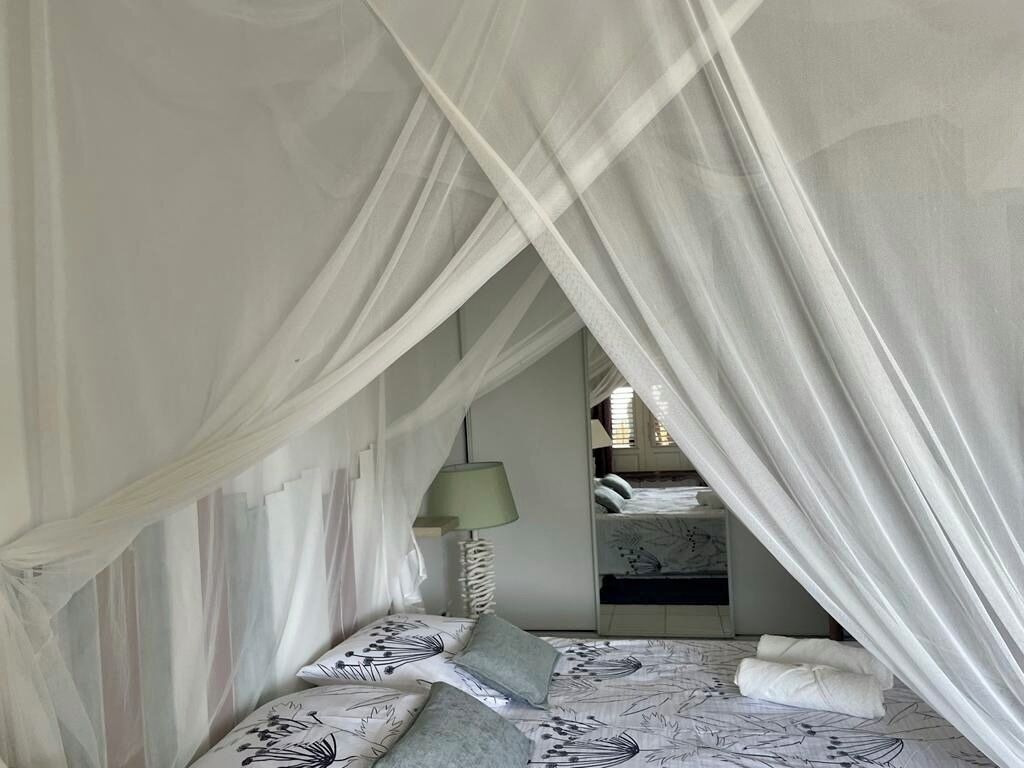 A bedroom with a canopy bed, a bedside lamp, and a view of a staircase.