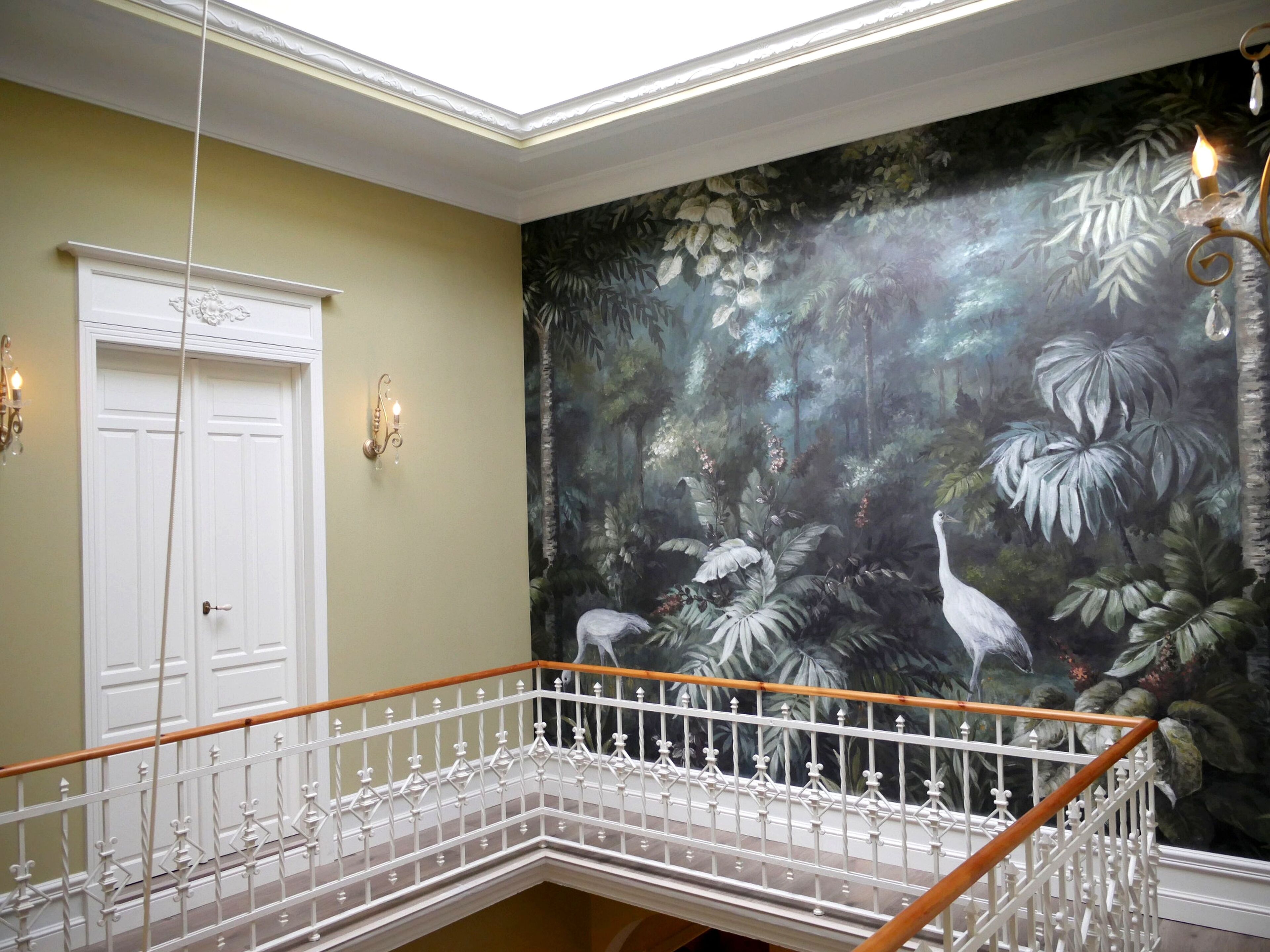 A staircase with white balusters and a wooden handrail, leading to a room with a mural of tropical foliage and birds.