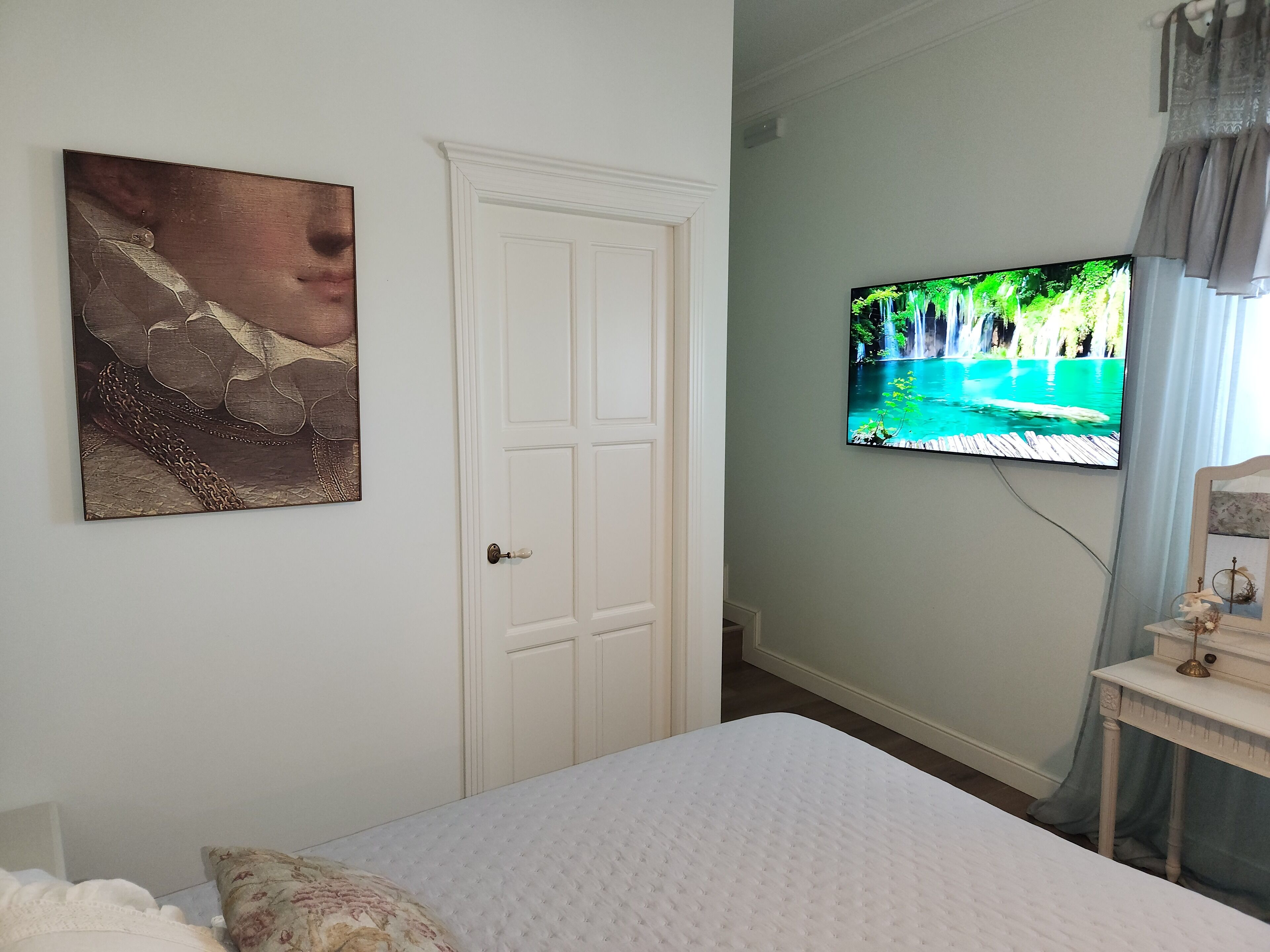 Un dormitorio con una cama, un televisor mostrando una escena natural y una puerta.