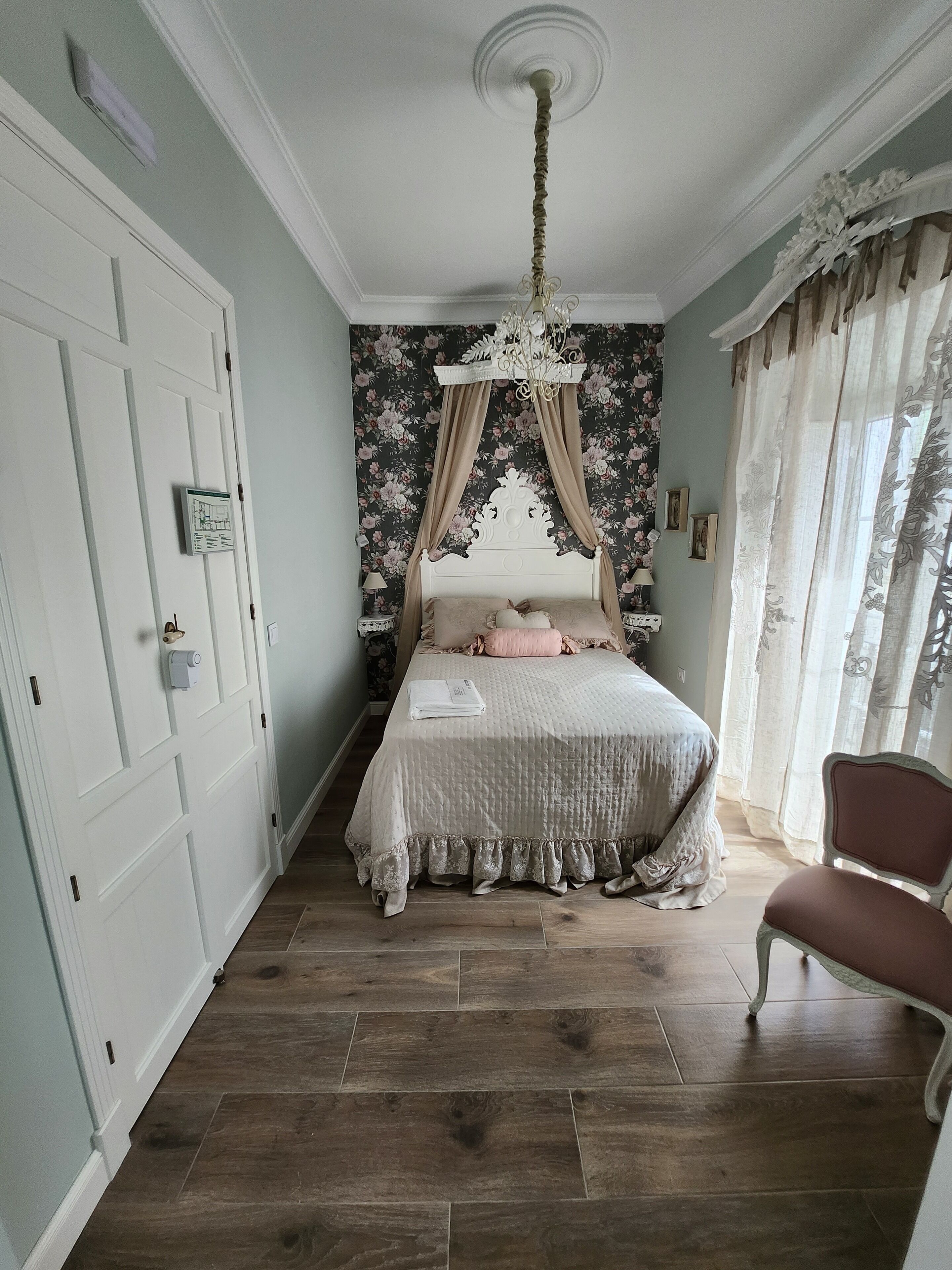 Un dormitorio con cama con dosel, una araña, piso de madera y una silla.