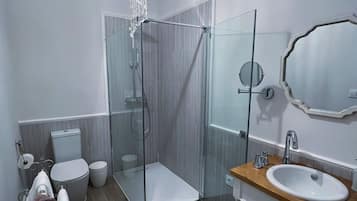 Un baño moderno con cabina de ducha de vidrio, tocador de madera, espejo grande y candelabro.