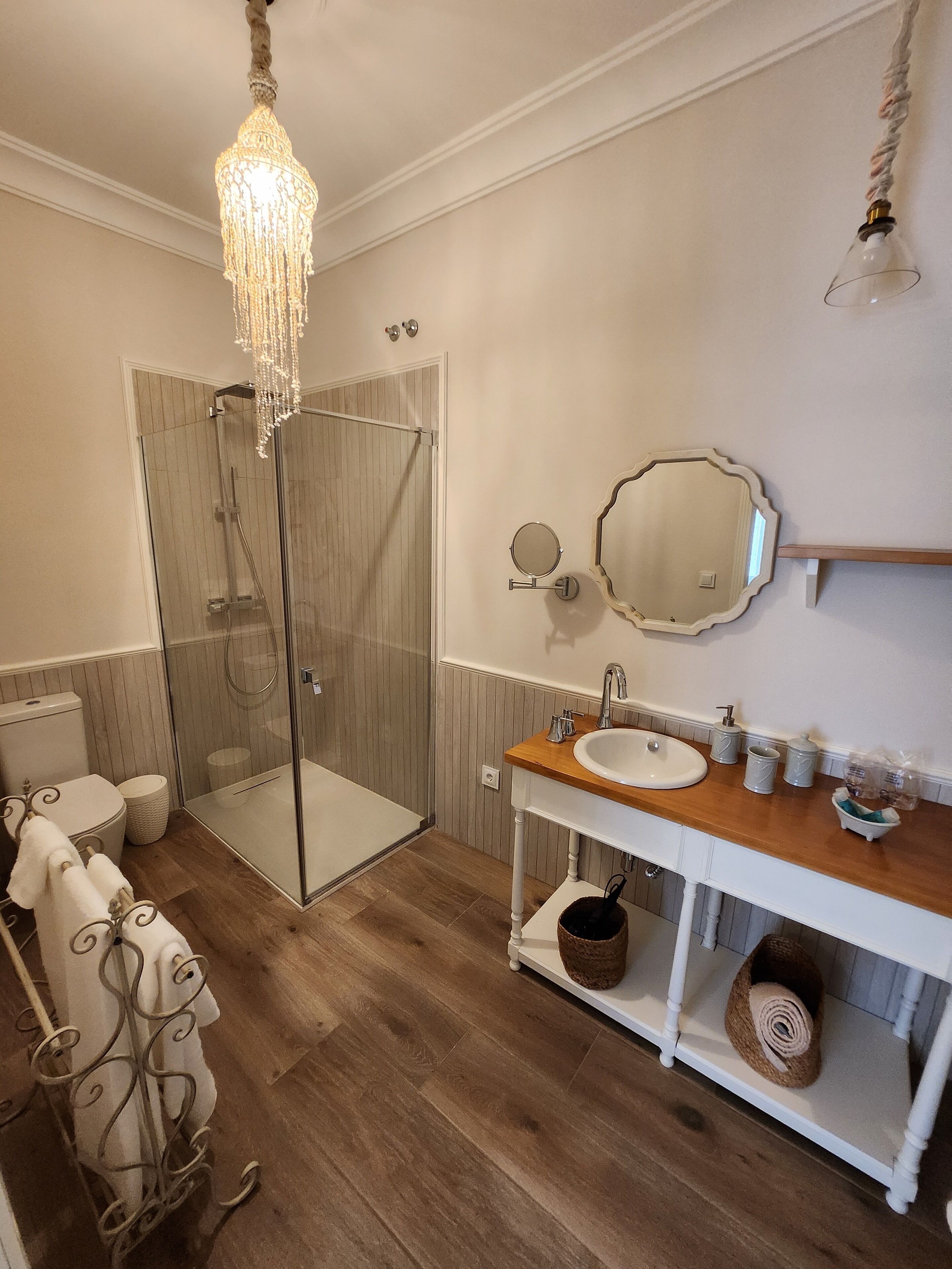 Un baño con ducha de vidrio, tocador de madera, espejo redondo y candelabro.