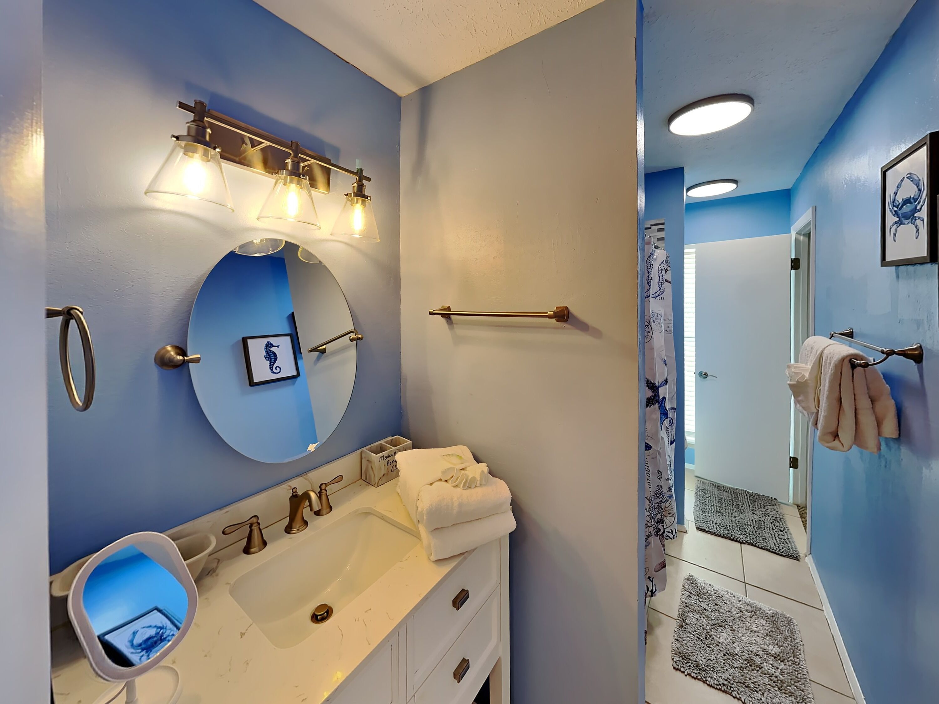 A bathroom with a round mirror, a sink with a vanity, a towel rack, and a shower area with a curtain.