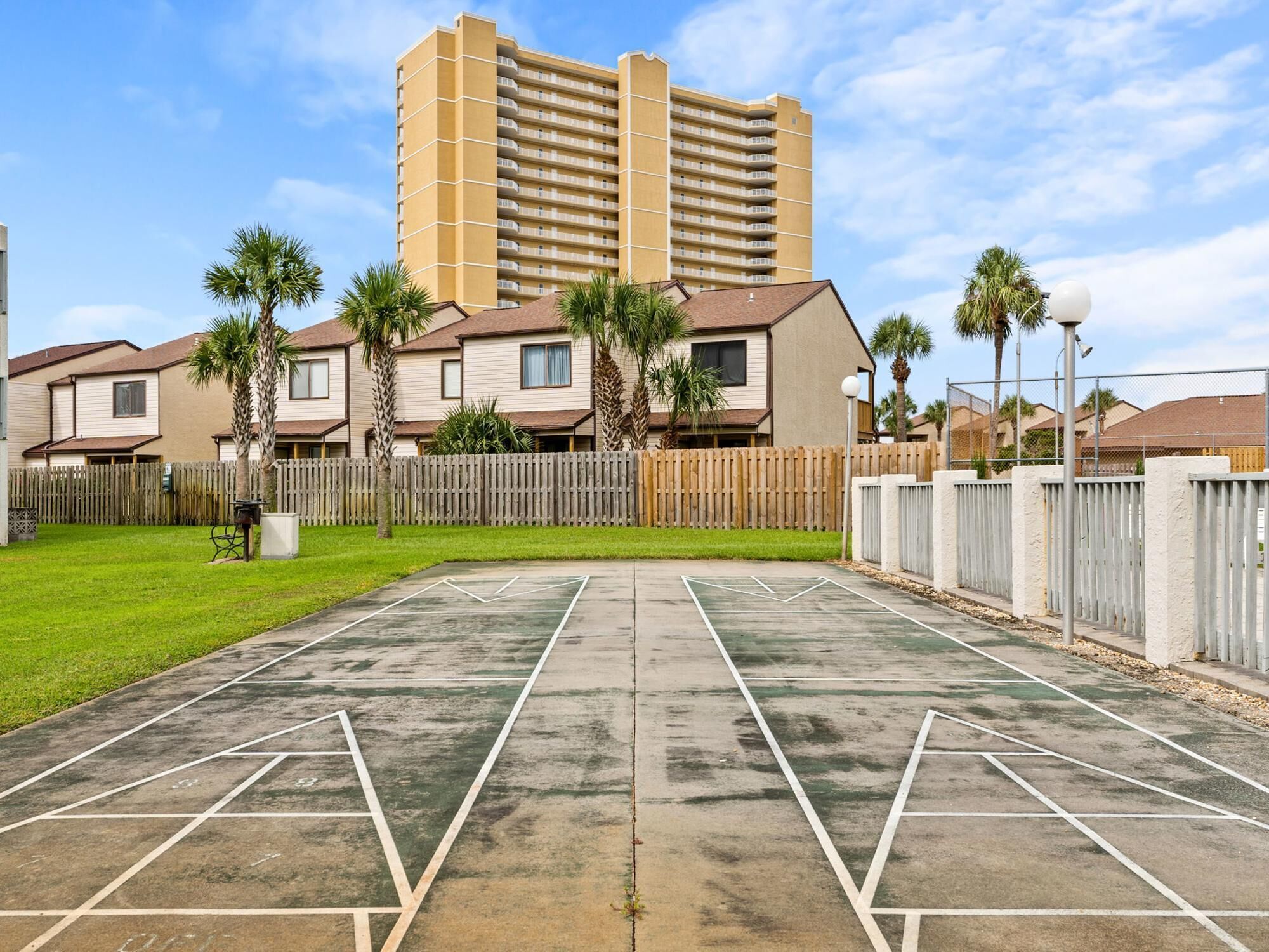 Un quartier résidentiel avec un court de tennis, une clôture en bois et un grand immeuble en arrière-plan.