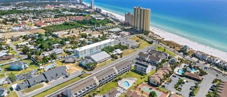 An aerial view of a coastal resort area with beachfront properties, a large hotel complex, and a swimming pool.