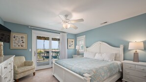 A bedroom with a bed, a nightstand, a dresser, a ceiling fan, and a view of the outdoors.