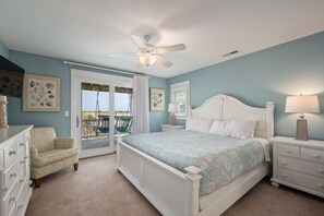A bedroom with a bed, a nightstand, a dresser, a ceiling fan, and a view of the outdoors.