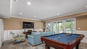 A pool table, a sofa, and a television in a room with beige walls and a tiled floor.